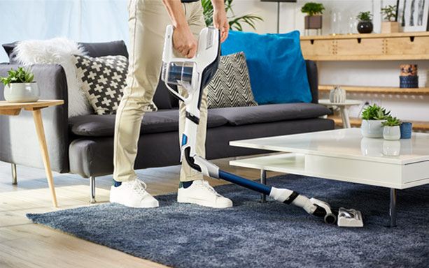 Une personne aspire sous la table basse sans encombre grâce au tube flexible